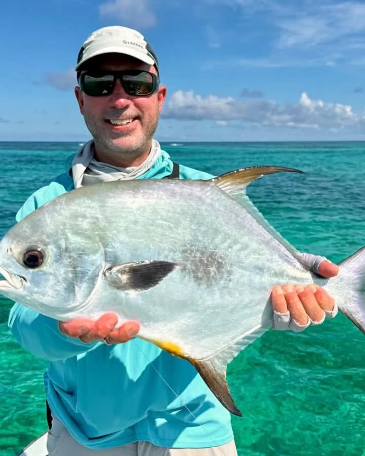 An angler holding a permit over bright turquoise flats