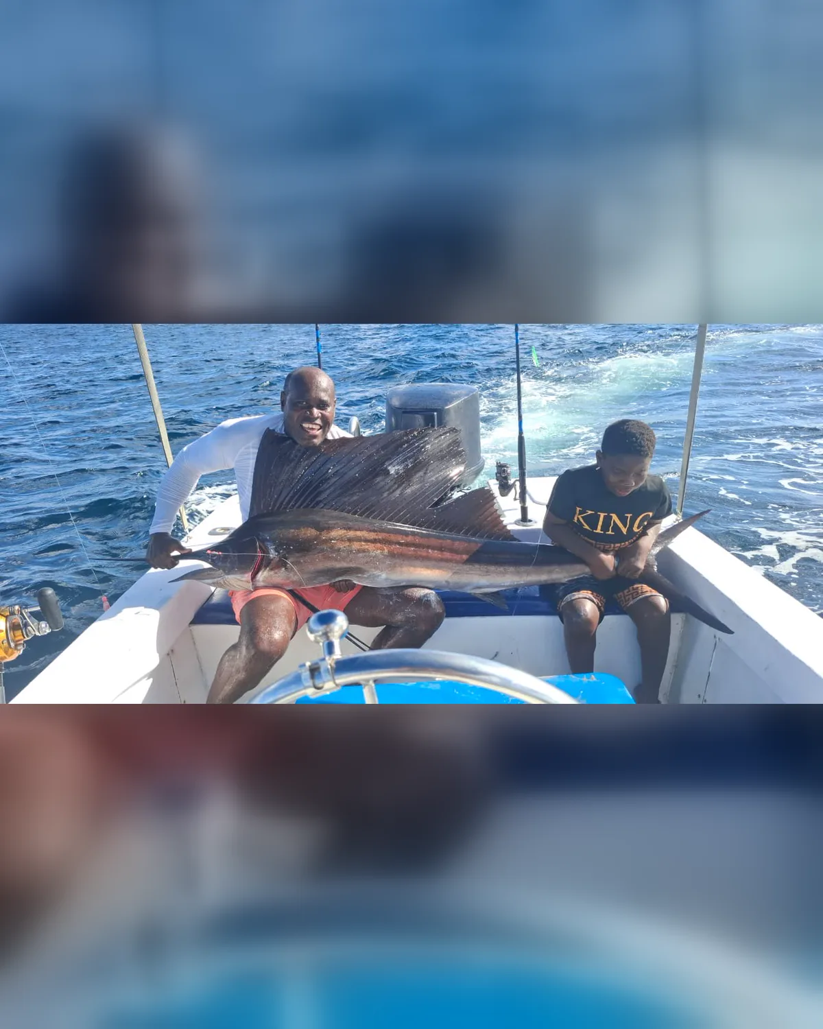 A man and a boy holding a sailfish across the stern, both grinning