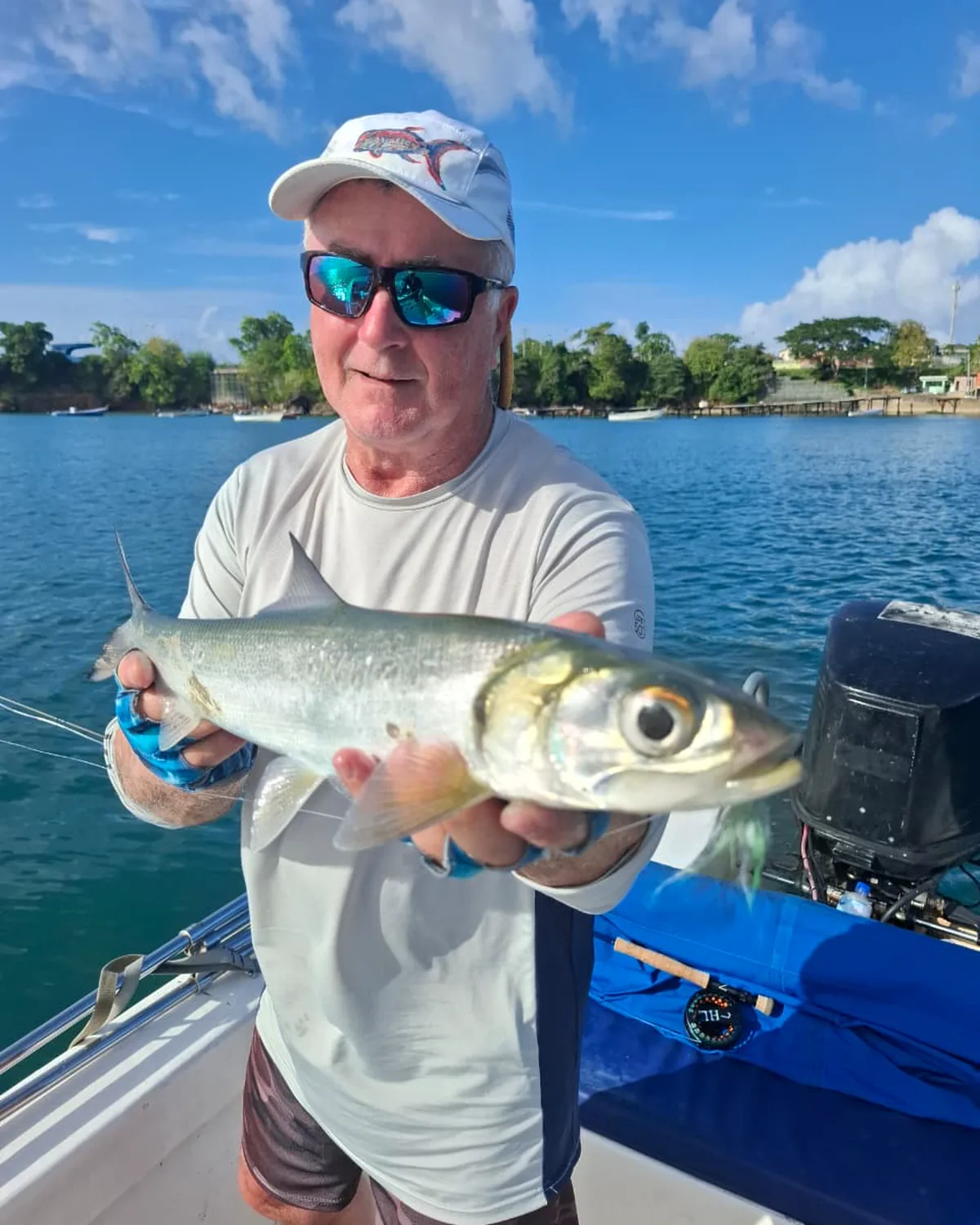 A tarpon held up on the boat with the Buccoo shoreline behind