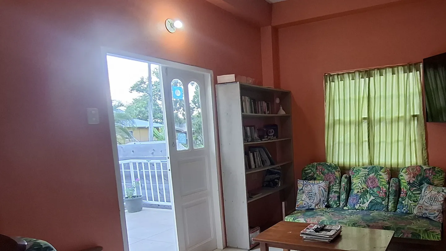 The apartment's living room, two settees and a wall-mounted television, with the balcony door open