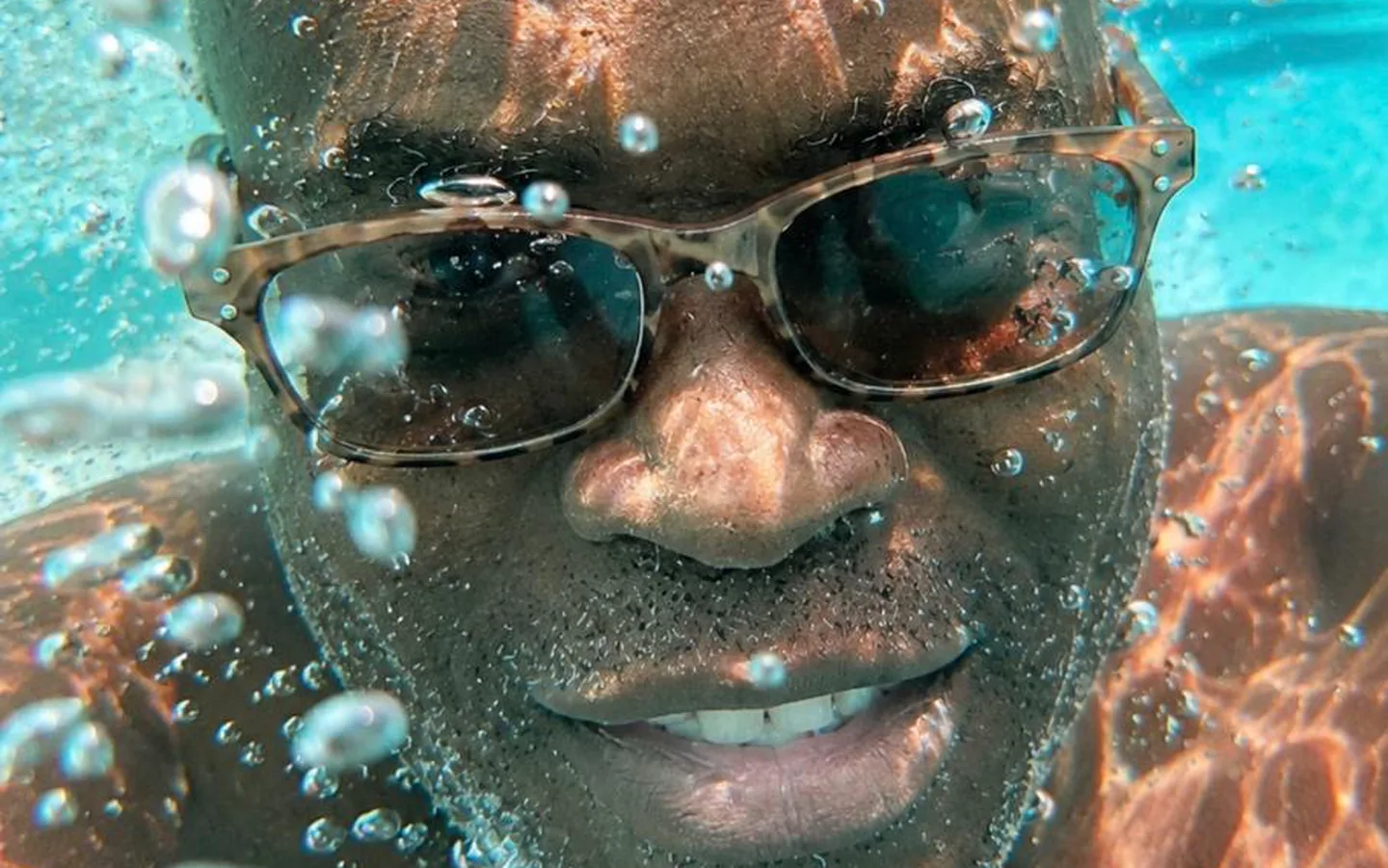 A snorkeler grinning underwater through a stream of bubbles
